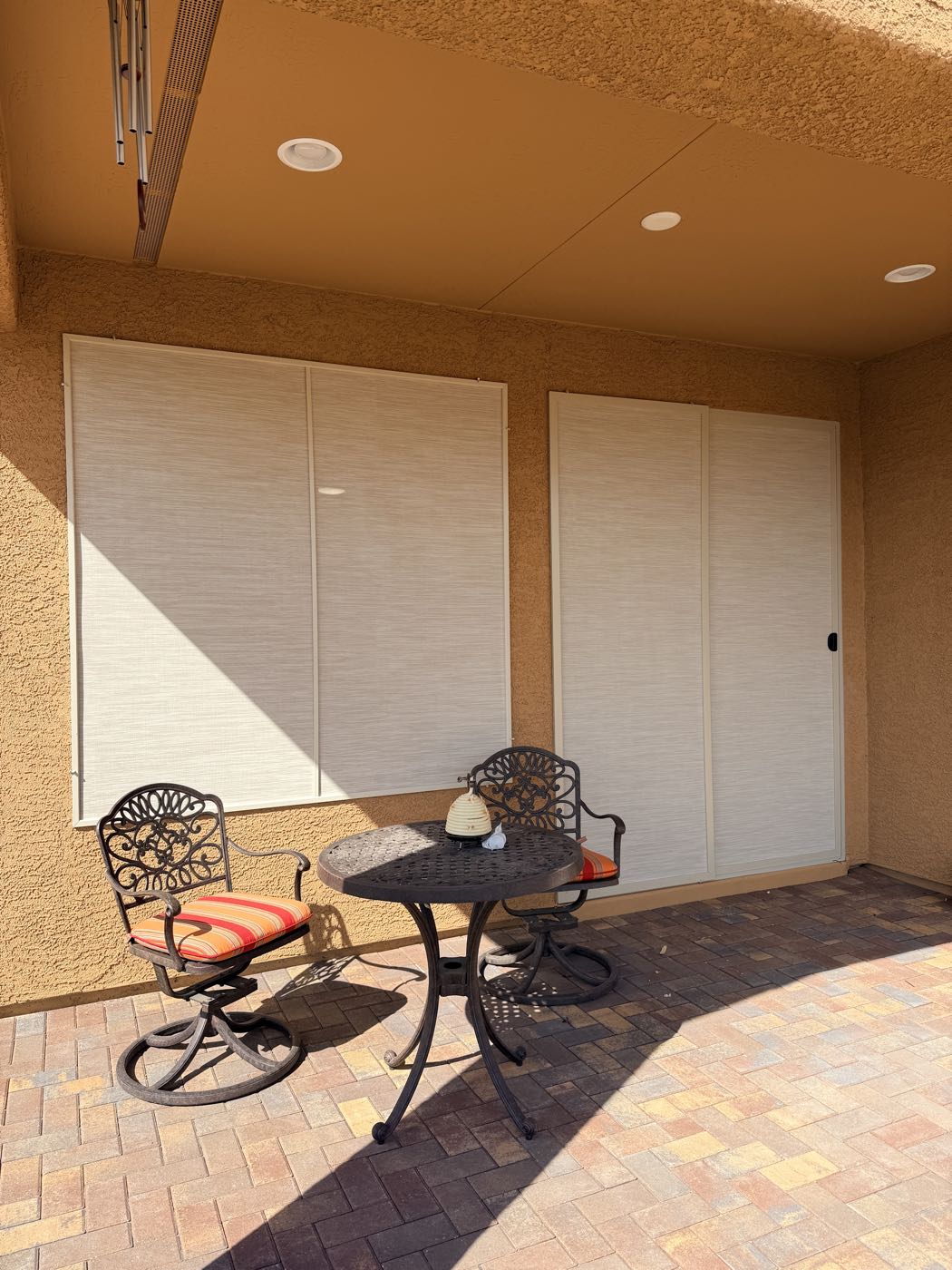 A shaded patio with two large solar screens behind a bistro table