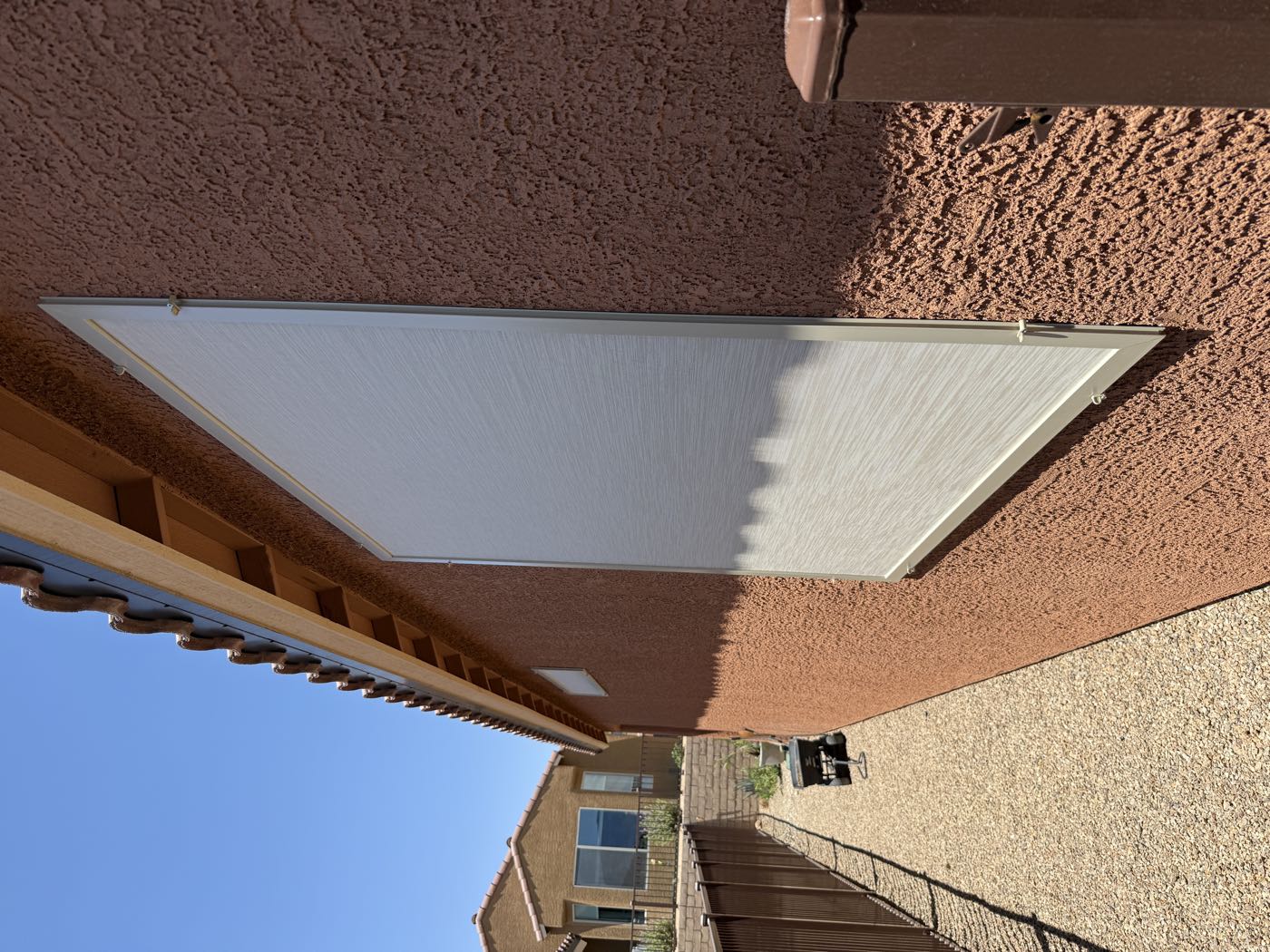A freshly installed light solar screen on a red stucco home under full desert sun